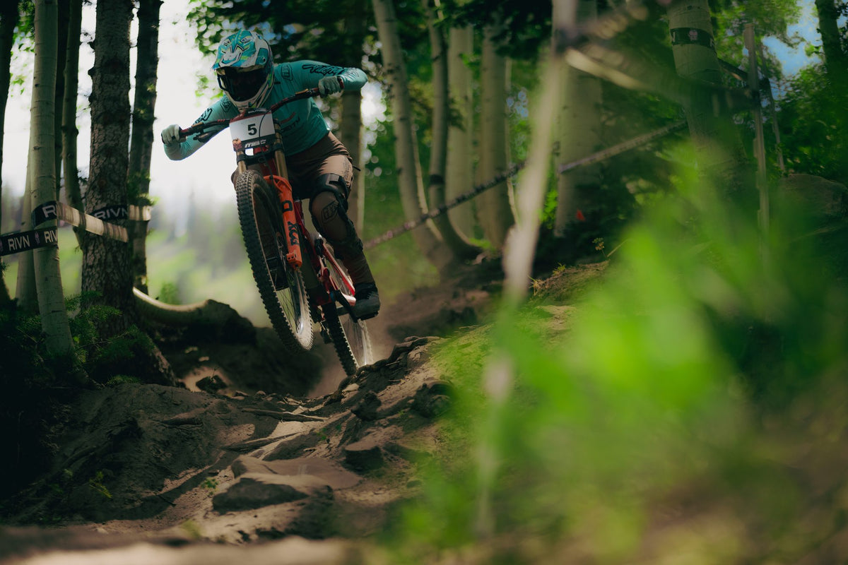 A rider on an orange bike drops through the trees at Solitude