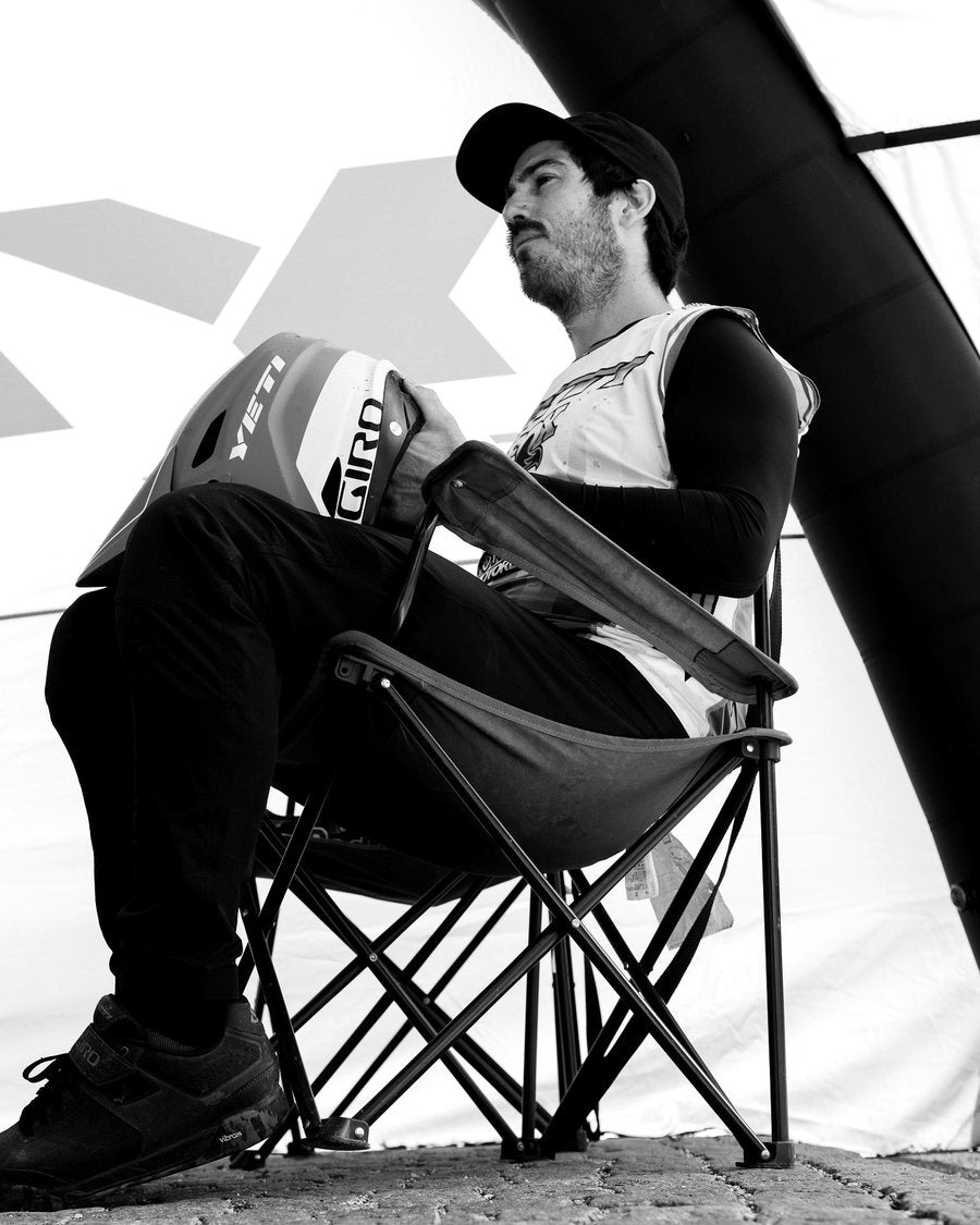 Shawn Neer, the Series Director, in a chair at the tent with a helmet in his hands, in black and white